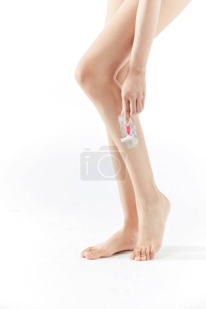 Téléchargez les photos : Plan vertical d'une femme se rasant les jambes avec un rasoir isolé sur fond blanc - en image libre de droit