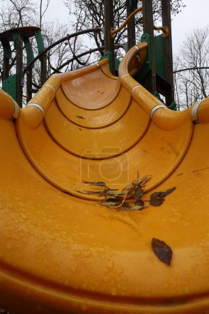 Foto de Una toma vertical de un tobogán húmedo amarillo y columpiarse en un parque con hojas de otoño en él - Imagen libre de derechos
