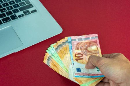 Téléchargez les photos : Les mains caucasiennes tenant des billets en euros près d'un ordinateur portable - en image libre de droit