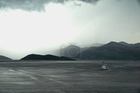 Foto de Una pintoresca vista de un yate flotando a las colinas bajo el rayo con nubes tormentosas brumosas - Imagen libre de derechos