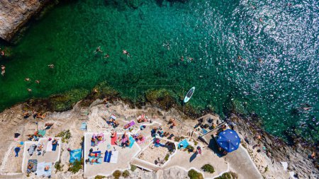 Téléchargez les photos : Une antenne de personnes en vacances posées sur des serviettes sur la plage et quelques baignades dans la mer turquoise - en image libre de droit
