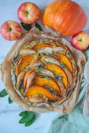 Photo for A closeup of pumpkin quiche on the table, apples and pumpkin around in the blurred background - Royalty Free Image