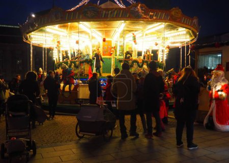 Téléchargez les photos : Une vue de nuit sur le marché de Noël, un Père Noël et les personnes avec enfants et poussettes autour du carrousel illuminé en Allemagne - en image libre de droit