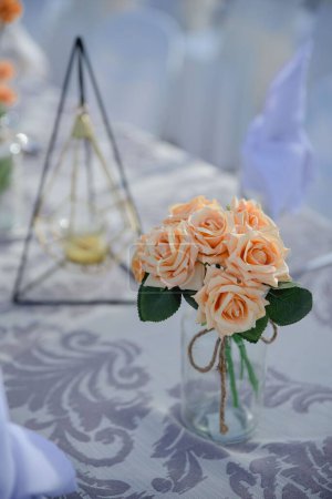 Photo for A vertical closeup shot of a small vase with beautiful peach-colored flowers placed on a table - Royalty Free Image
