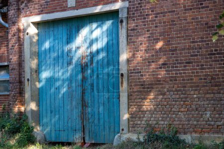 Téléchargez les photos : Une vieille porte bleue altérée dans un mur de briques rouges capturé avec les aperçus de la lumière du soleil dessus - en image libre de droit