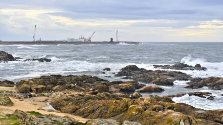 Téléchargez les photos : Un paysage marin rocheux pittoresque avec la ville industrielle en arrière-plan - en image libre de droit