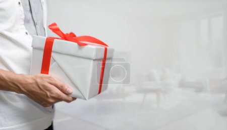 Téléchargez les photos : Mise au point sélective d'un homme tenant un cadeau avec un arc, dans une pièce blanche, le concept de donner des cadeaux pour le Nouvel An, anniversaires, et d'autres occasions - en image libre de droit