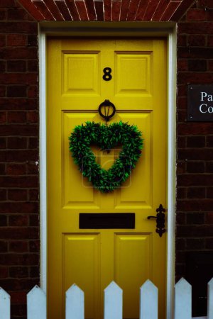 Foto de Un disparo vertical de una puerta amarilla con una corona de Navidad en forma de corazón. - Imagen libre de derechos