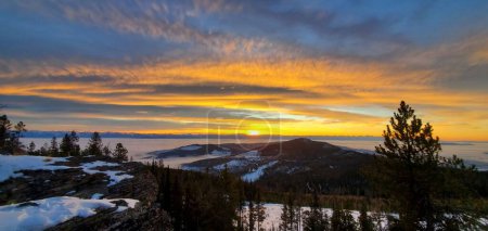 Foto de Un plano panorámico de montañas, árboles y nieve bajo el brillante cielo mágico naranja y azul - Imagen libre de derechos