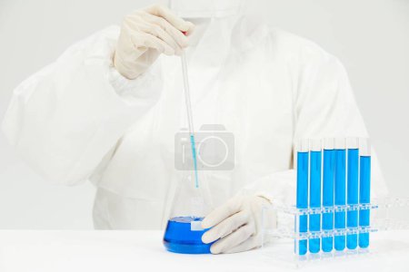 Foto de Un médico que trabaja en tubos de ensayo llenos de líquido azul sobre la mesa en un laboratorio médico - Imagen libre de derechos