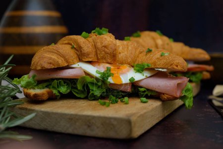 Photo for A closeup of a croissant sandwich with bacon and egg on a board - Royalty Free Image