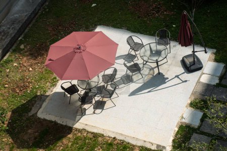 Foto de Una toma de alto ángulo de sillas y mesas bajo un paraguas en un parque verde - Imagen libre de derechos
