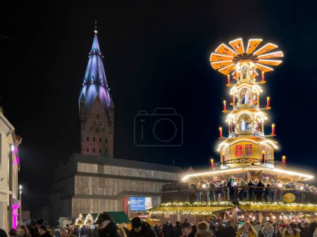 Téléchargez les photos : Marché de Noël le soir sur la place de la cathédrale. Une grande pyramide de Noël se dresse devant la cathédrale. Les gens célèbrent. - en image libre de droit