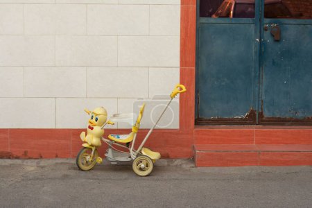 Foto de Una pequeña bicicleta para niños contra la pared de un edificio junto a una puerta metálica oxidada - Imagen libre de derechos
