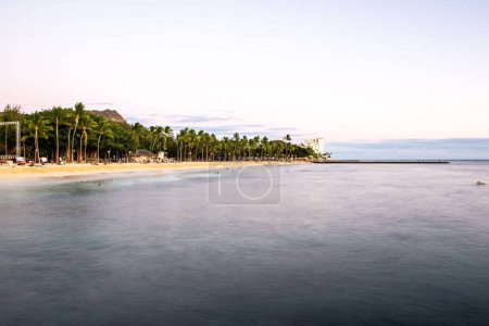 Photo for A beautiful scene of the clear ocean with a sandy beach full of palms and people near the buildings in Waikiki, Hawaii - Royalty Free Image