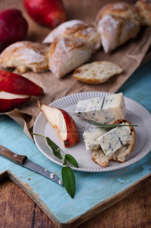 Foto de Rollos de baguette frescos rústicos en la tabla de cortar con peras y queso Gorgonzola - Imagen libre de derechos