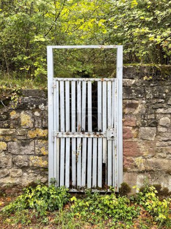 Téléchargez les photos : Un plan vertical de la vieille porte blanche rouillée sur le mur de pierre dans le parc pendant la journée - en image libre de droit