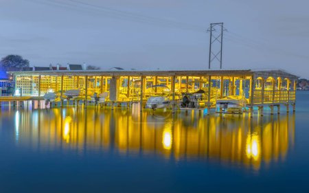 Foto de El muelle de madera iluminado con barcos reflejados en la superficie del agua. - Imagen libre de derechos