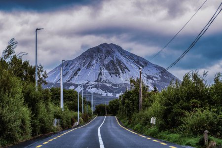 Téléchargez les photos : La route entourée d'arbres mène à la montagne Errigal par une journée nuageuse - en image libre de droit