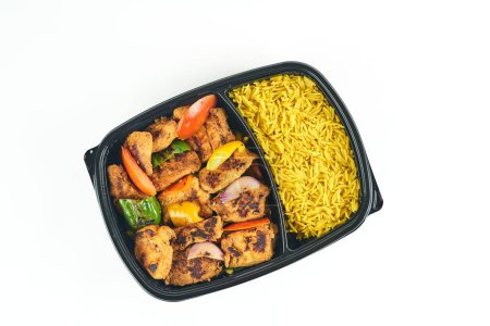 Foto de Una vista superior de la caja de plástico negro con arroz sartén amarilla y pollo a la parrilla y pimientos sobre fondo blanco - Imagen libre de derechos
