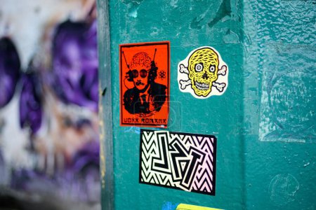 Téléchargez les photos : Un poteau avec des autocollants dessus avec un graffiti crâne violet en arrière-plan à Glasgow en Écosse - en image libre de droit