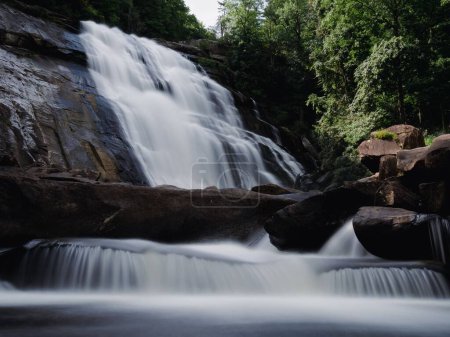Téléchargez les photos : Une belle cascade soyeux coule sur les rochers et dans la rivière ci-dessous - en image libre de droit