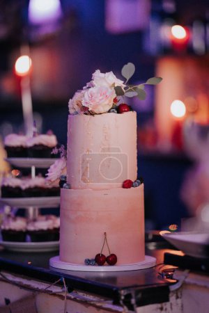 Foto de Un plano vertical de un pastel de bodas, decorado con rosas y frutas rosadas, y luces bokeh en el fondo - Imagen libre de derechos