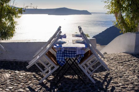 Téléchargez les photos : Une table avec des assiettes et des chaises en bois à l'extérieur par beau temps à Oia, Santorin - en image libre de droit