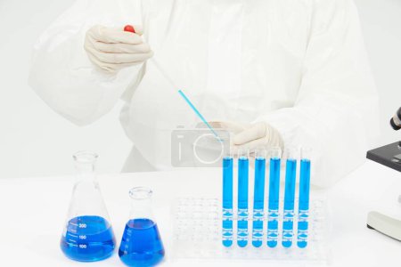 Téléchargez les photos : Un médecin travaillant sur des éprouvettes remplies de liquide bleu sur la table dans un laboratoire médical - en image libre de droit