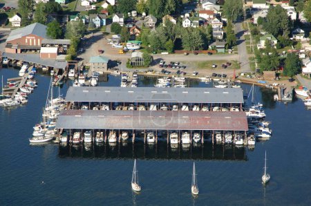 Téléchargez les photos : Vue aérienne d'un quai rempli de bateaux et de yachts avec une petite ville en arrière-plan par une journée ensoleillée - en image libre de droit