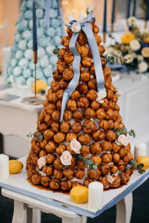 Photo for A vertical shot of a tasty croquembouche decorated with flowers on the table with candles - Royalty Free Image