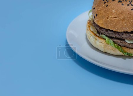 Foto de Un primer plano de una hamburguesa en un plato sobre fondo azul - Imagen libre de derechos