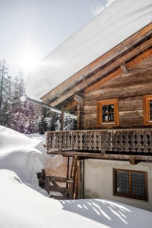 Foto de Un plano vertical de una casa de madera cubierta de nieve con montañas al fondo en un día soleado - Imagen libre de derechos