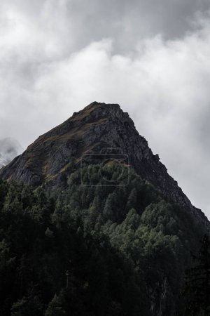 Photo for A vertical shot of a mountain covered in forests with a dramatic cloudy sky in the background - Royalty Free Image