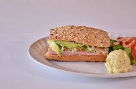 Photo for A close-up shot of a sandwich with ham and avocado served with a side salad and scrambled eggs - Royalty Free Image