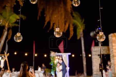 Foto de Un enfoque selectivo en las luces colgantes como los recién casados marido y mujer están bailando en el fondo - Imagen libre de derechos