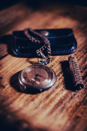 Téléchargez les photos : Une verticale d'une montre de poche vintage attachée à un portefeuille en cuir sur une surface en bois - en image libre de droit