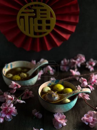 Foto de Un primer plano vertical de cuencos de Tangyuan sobre una mesa decorada con flores rosadas. - Imagen libre de derechos