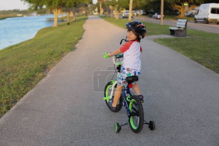 Téléchargez les photos : Un jeune garçon avec un casque à vélo avec des roues d'entraînement. - en image libre de droit