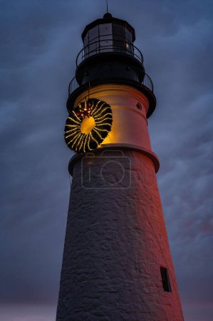 Photo for A vertical low angle shot of the Portland Head Light lighthouse at sunrise with a holiday wreath - Royalty Free Image