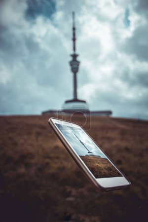 Photo for A flying phone screen with a television tower both on screen and in the background, vertical - Royalty Free Image