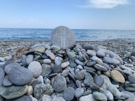 Téléchargez les photos : Un tas de rochers avec une croix sur l'une des pierres avec la mer calme en arrière-plan - en image libre de droit