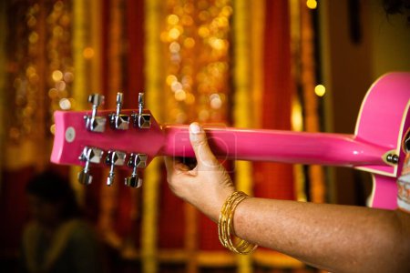 Foto de Un primer plano de una mano sosteniendo una guitarra rosa con un fondo borroso - Imagen libre de derechos