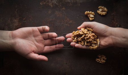 Foto de Una vista superior de manos humanas compartiendo nueces en superficie oxidada - Imagen libre de derechos