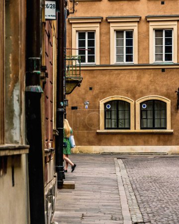 Photo for A vertical of a blonde woman in a green dress walking in the streets of the old town in Warsaw - Royalty Free Image