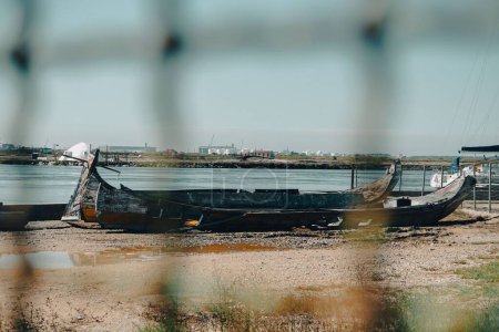 Téléchargez les photos : Une belle vue des bateaux en bois cassés sur le littoral pris à travers la maille de corde - en image libre de droit