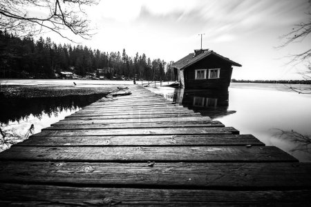 Photo for A grayscale of wooden pier land with rural Drunken Sauna in the water with forest trees - Royalty Free Image