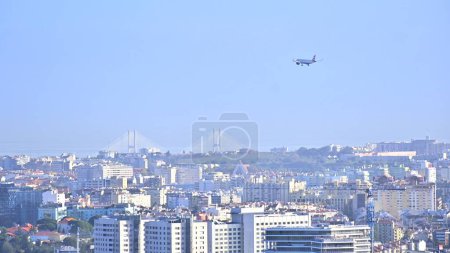Photo for A picturesque shot of a commercial aircraft flying over city buildings on sunny day under blue sky - Royalty Free Image