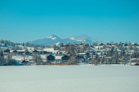 Photo for The snow-covered field before the town buildings and slopes under the blue sky - Royalty Free Image