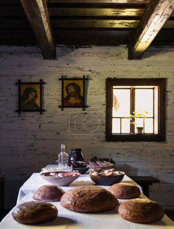 Téléchargez les photos : Une salle rurale avec du pain sur la table et des photos de saints sur le mur près de la fenêtre - en image libre de droit